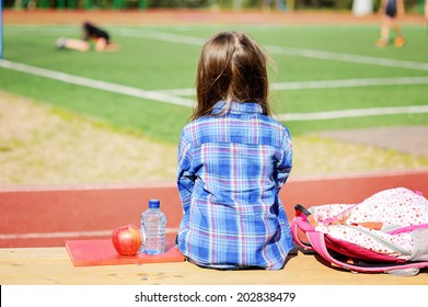 Beauty  Fashion Brunette School Age Kid Girl In The Blue Plaid Shirt, Jeans Skirt And Yellow Scarf Writing In Her Notepad Outdoor On The Playground