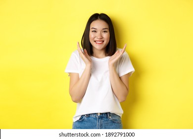 Beauty And Fashion Concept. Excited Asian Woman Clap Hands And Smiling Happy At Camera, Standing In White T-shirt Against Yellow Background