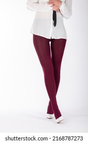 Beauty and fashion concept. Woman beautiful legs wearing burgundy color tights and classic white high heel shoes on white studio background with copy space. Models with white shirt and black ties