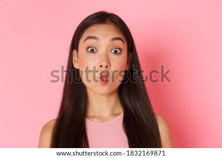Beauty, fashion and lifestyle concept. Portrait of funny and playful, silly asian girl looking surprised and sucking lips, making fish mouth as fooling around, standing over pink background