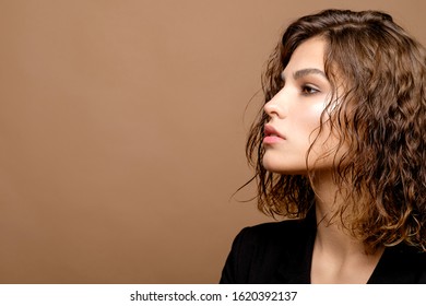 beauty fashion model with clean skin and curly hair in black jacket on biege background, serious business woman, copy space