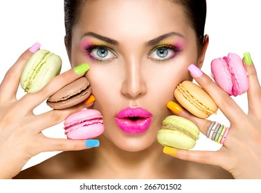 Beauty fashion model girl with colourful makeup and manicure taking colorful macaroons. Beautiful woman, bright make-up. Purple lipstick, vivid eyeshadow and accessories. Diet, dieting concept. Sweets