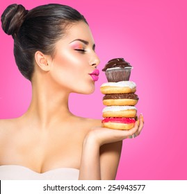 Beauty fashion model girl taking sweets and colorful donuts. Funny joyful Vogue styled woman with sweets on pink background. Diet, dieting concept. Junk food, Slimming, weight loss