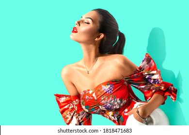 Beauty fashion model girl in trendy wear, with bright make-up, brunette woman over blue background posing. Street Fashion look. Beautiful young brunette woman with trendy accessories