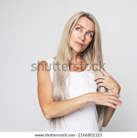 Beauty, fashion and old people concept: beautiful elderly woman touch long lovely grey hair over light grey background.