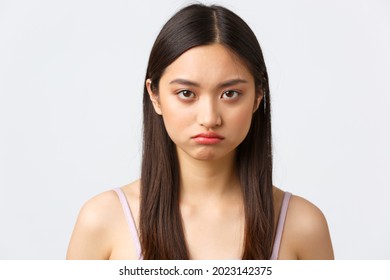 Beauty, fashion and people emotions concept. Close-up portrait of gloomy pouting cute asian girl, frowning offended or insulted, standing bothered over white background - Shutterstock ID 2023142375