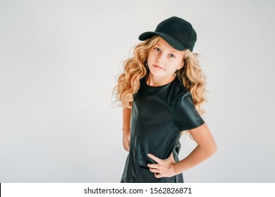 Beauty fashion portrait of smiling curly hair tween girl in black leather dress and baseball cap on the white background 