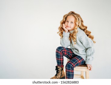 Beauty Fashion Portrait Of Smiling Curly Hair Tween Girl In Cozy Knitted Sweater And Plaid Pants On White Background 