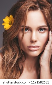 Beauty fashion portrait of young blond woman model with natural makeup and perfect skin with bright yellow chrysanthemum flower posing in studio
