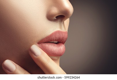 Beauty Fashion woman lips with natural Makeup and beige Nail polish. Matte lipstick and nails. Beauty girl face close up. Nude Colors. Sexy lips, Manicure, Make up. Over brown background.