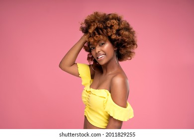 Beauty female colorful portrait of happy smiling attractive afro woman with curly hairstyle and glamour summer makeup. Pink pastel studio background. A lot of copy space.