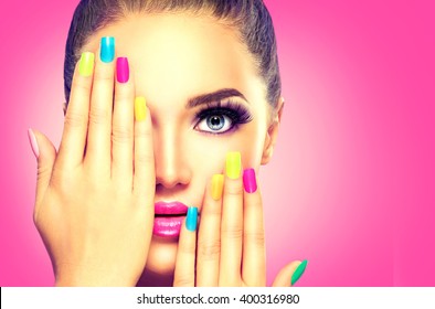 Beauty Girl Face with Colorful Nail polish. Colourful Studio Shot of young Woman. Vivid Colors. Colourful Manicure and fashion Makeup. Rainbow Colors. Beautiful lady touching her face