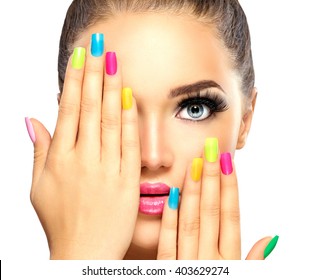Beauty Girl Face with Colorful Nail polish. Colourful Studio Shot of young Woman. Vivid Colors. Colourful Manicure and fashion Makeup. Rainbow Colors. Beautiful lady touching face. Isolated on white