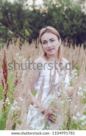 Beauty Girl Outdoors enjoying nature. Beautiful Teenage Model girl in white dress jumping on summer Field with blooming wild flowers, Sun Light. Free Happy Woman. Toned in warm colors