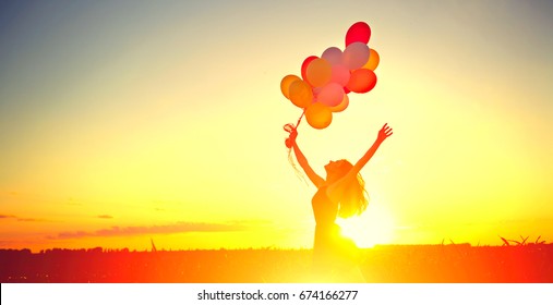 Beauty Girl Running And Jumping On Summer Field With Colorful Air Balloons Over Sunset Clear Sky. Silhouette, Happy Young Healthy Woman Enjoying Nature Outdoors. Running And Jumping Female. Flying