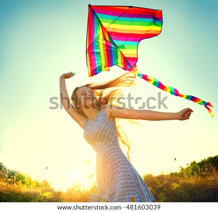 Beauty girl in short dress running with kite on the field. Beautiful young woman with flying colorful kite over clear blue sky. Free, freedom concept. Emotions, healthy lifestyle