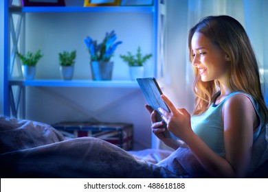 Beauty Girl using tablet pc in her bed at night. Beautiful young woman with tablet computer  lying in her comfortable bed in a dark room, watching movie, playing game, reading or chatting - Powered by Shutterstock