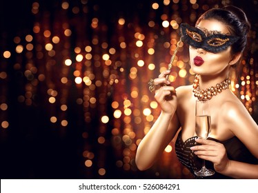 Beauty Glamour Woman Celebrating With Champagne, Wearing Carnival Mask. Party, Drinking Champagne Over Holiday Glowing Background. Christmas And New Year Celebration