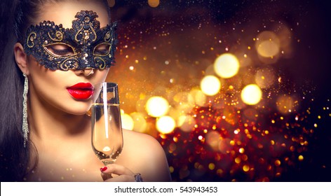 Beauty Glamour Woman Celebrating With Champagne, Wearing Carnival Mask. Party, Drinking Champagne Over Holiday Glowing Background. Christmas And New Year Holiday Celebration.