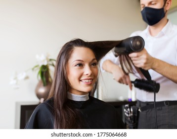 beauty, hairdressing and health safety concept - young woman wearing face protective medical mask for protection from virus disease and hairdresser with fan making hot styling at hair salon