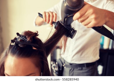 beauty, hairstyle, blow-dry and people concept - close up of young woman and hairdresser with fan and brush making hot styling at hair salon