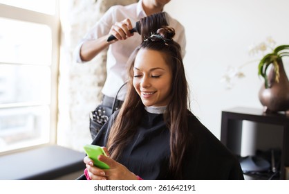 beauty, hairstyle and people concept - happy young woman with smartphone and hairdresser making hair styling at salon - Powered by Shutterstock