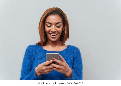 Beauty Happy African Woman In Sweater Looking At Phone And Writing Message. Isolated Gray Background