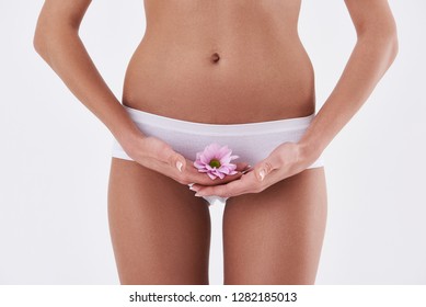 Beauty and health. Close up of well-shaped woman in white panties covering intimate area with flower