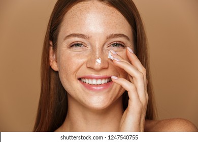 Beauty Image Of Pretty Shirtless Woman Smiling And Applying Face Cream Isolated Over Beige Background