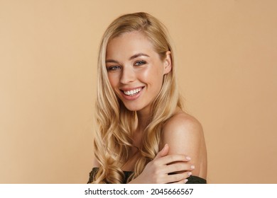 Beauty image of a smiling happy young blonde woman with long hair naked shoulders standing over beige background