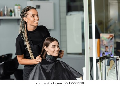 beauty industry, positivity, happy hair stylist with braids wearing hairdressing cape on female client, hair extension, hair treatment, salon customer, beauty profession - Powered by Shutterstock