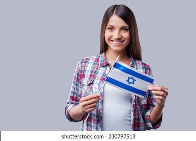 Beauty With Israeli Flag. Happy Young Women Holding Flag Of Israel While Standing Against Grey Background