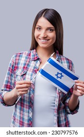 Beauty With Israeli Flag. Happy Young Women Holding Flag Of Israel While Standing Against Grey Background