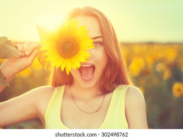 Beauty joyful teenage girl with sunflower enjoying nature and laughing on summer sunflower field. Sunflare, sunbeams, glow sun. Backlit.