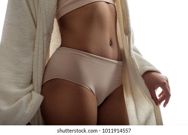 Beauty lines. Close up of female body wearing high-waist panties. She is standing in robe and showing her flat stomach. Isolated on background