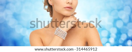 beauty, luxury, people, holidays and jewelry concept - close up of beautiful woman with pearl earrings and bracelet over blue lights background
