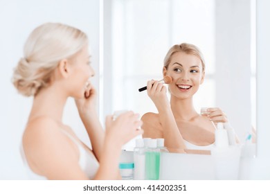 Beauty, Make Up, Cosmetics, Morning And People Concept - Smiling Young Woman Makeup Brush And Powder Foundation Looking To Mirror At Home Bathroom