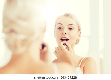 Beauty, Make Up, Cosmetics, Morning And People Concept - Smiling Young Woman With Lipstick Applying Makeup And Looking To Mirror At Home Bathroom