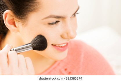 beauty, make up, cosmetics and people concept - close up of smiling young woman face applying blush with makeup brush