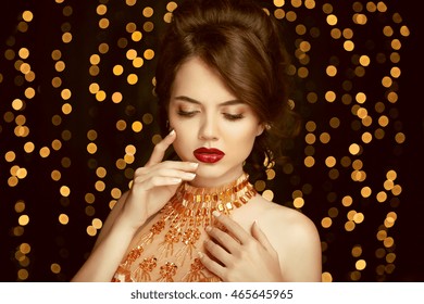 Beauty Makeup. Glamour Woman With Perfect Skin Portrait. Beautiful Brunette Girl  Model With Red Lips In Golden Dress, Isolated On Christmas Party Lights Background.