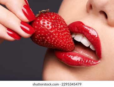 Beauty, makeup and woman with a strawberry in a studio with red nails and lipstick cosmetics. Health, wellness and closeup of a female model eating fruit for nutrition isolated by a gray background.