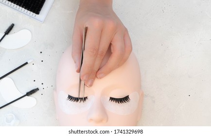 A Beauty Mannequin Training Head With A Person Practising Lash Extension Techniques.  Beauty Treatment Tools Arranged On Left Side Of Background Frame. 