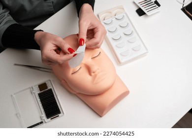 A beauty mannequin training head with a person practicing lash extension techniques. Female hands preparing glue cotton tape under eye. Basic training to build eyelashes. Copy space