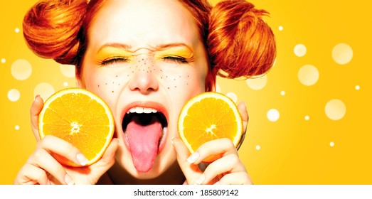 Beauty Model Girl with Juicy Oranges. Beautiful Joyful teen girl with freckles, funny red hairstyle and yellow makeup. Open mouth. Professional make up. Orange  Slices 