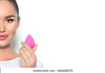 Beauty model girl, makeup artist holding pink make up blender sponge and smiling. Beautiful brunette young woman with nude make-up. Perfect skin closeup. Face contouring makeup. On white.