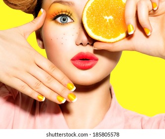 Beauty Model Girl takes Juicy Oranges. Beautiful Joyful teen girl with freckles, funny red hairstyle, yellow makeup and nails. Professional make up. Orange Slices.  