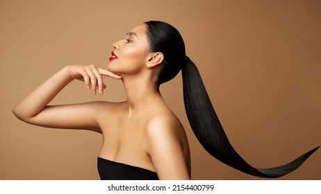 Beauty Model Profile. Young Woman with long Ponytail Hair. Women Face Side view over beige background. Lady with Red Lipstick and Black Straight Tail Hairstyle