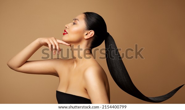 Beauty Model Profile. Young Woman\
with long Ponytail Hair. Women Face Side view over beige\
background. Lady with Red Lipstick and Black Straight Tail\
Hairstyle