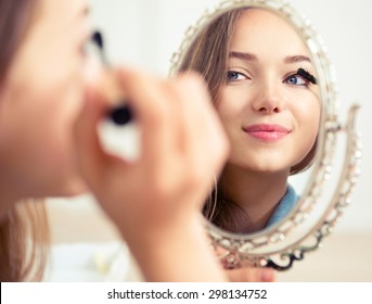 Beauty Model Teenage Girl Looking In The Mirror And Applying Mascara Make Up. Beautiful Young Woman Apply Makeup