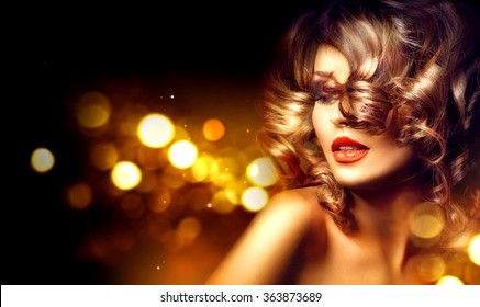 Beauty model woman with beautiful make up and curly hair style over holiday dark background with magic glow. Holiday celebration. Brunette Glamour lady with perfect make up and hairstyle